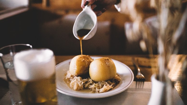 Bekannt für verschiedene gefüllte Erdäpfelknödel, © Niederösterreich Werbung/Mara Hohla Zwei Erdäpfelknödel auf Sauerkraut mit Soße übergossen.