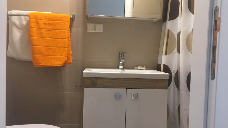 Bad, Privatzimmer Jarosch, Tulln, © Familie Jarosch Kleines Badezimmer mit Waschbecken, Spiegel, Duschvorhang und Handtüchern.