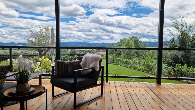 Terrasse Johannesbachklamm Chalet, © Johannesbachklamm Chalet Terrasse mit Holzboden, modernen Möbeln und Blick auf eine grüne Landschaft und Berge.