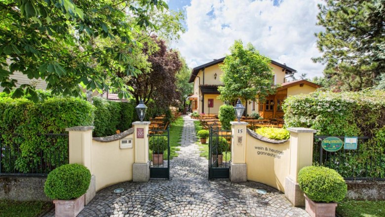 Einfahrt, © Wein und Heuriger Ganneshofer Eingang zu einem gemütlichen Gasthaus mit Garten und Sitzplätzen im Freien.