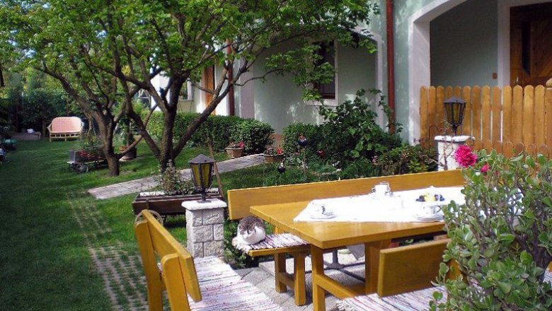 Garten, © Schwarzinger Ein gepflegter Garten mit Holzmöbeln, einer Katze auf der Bank und einem gedeckten Tisch.