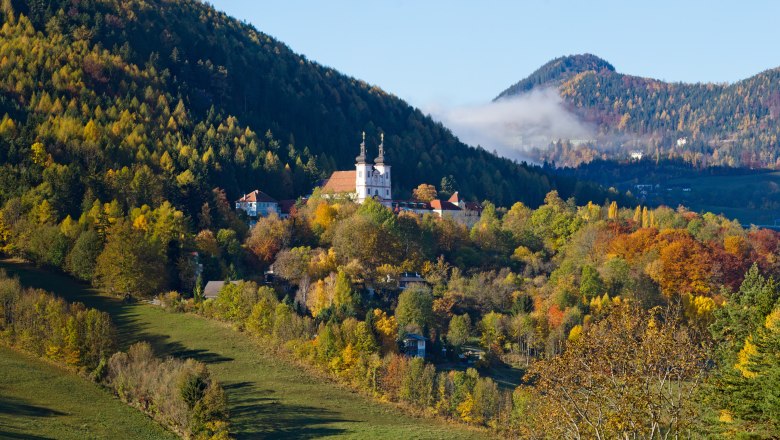 herbstliches Maria Schutz, © Fam. Auer GmbH Herbstliche Landschaft mit Kirche in Maria Schutz, umgeben von bunten Bäumen und Hügeln.