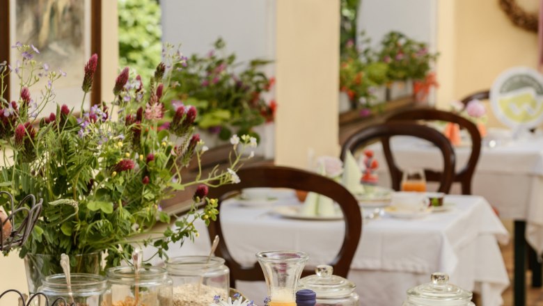 Frühstück im Prandtauerhof, © Rita Newman Ein reich gedeckter Frühstückstisch mit Brot, Aufschnitt, Gemüse, Saft und Blumen in einem eleganten Raum.