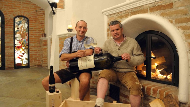 Küffer Keller Dürnstein, © Familie Thiery Zwei Männer in traditioneller Kleidung halten große Weinflasche vor Kamin.