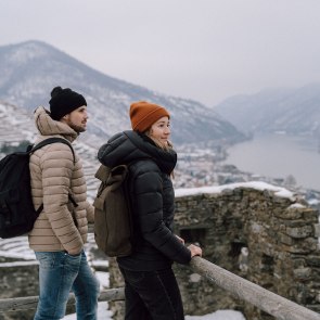 Aussicht auf die winterliche Wachau, © © Niederösterreich Werbung/Robin Uthe In der winterlichen Landschaft genießen zwei Wanderer die atemberaubende Aussicht auf die schneebedeckten Berge und das glitzernde Wasser des Flusses. Die frische, kalte Luft und die ruhige Atmosphäre laden dazu ein, die Schönheit der Natur in vollen Zügen zu erleben.