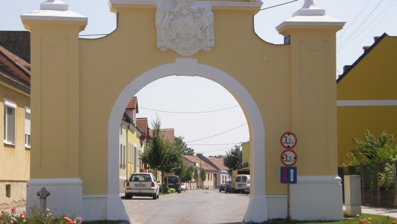 Oberes Tor, © Marktgemeinde Trautmannsdorf/L. Gelbes Tor mit Wappen, das eine Straße überspannt.