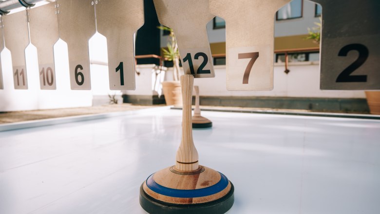 Eisstockschießen, © Sporthotel Semmering Eisstock auf einer glatten Fläche vor nummerierten Zielen.