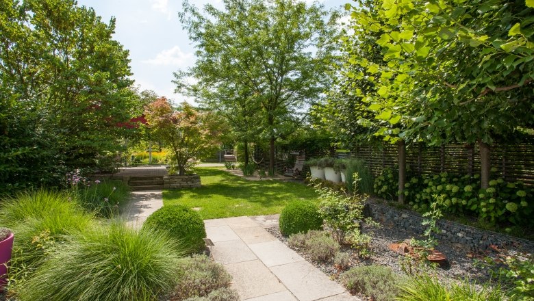 Chill out Garten, © Helmut Kail Ein gepflegter Garten mit Rasen, Bäumen und einem gepflasterten Weg.