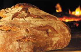 Biohof Prock, © Prock Ein frisch gebackenes Brot vor einem Holzofen mit Flammen.