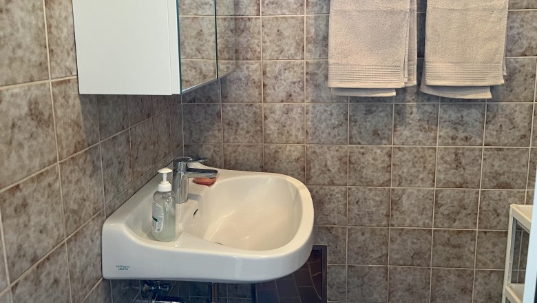 Bad, © Waltraud Forstner Ein Badezimmer mit Waschbecken, Spiegel, Handtüchern und Fliesen.