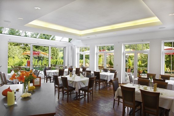 Gartenrestaurant, © Bauer & CO Ges.m.b.H. Innenansicht eines hellen Restaurants mit großen Fenstern und gedeckten Tischen.