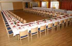 Festsaal, © Gasthof Klang Ein großer Festsaal mit U-förmig gedeckten Tischen, dekoriert mit roten Servietten und Blumen.