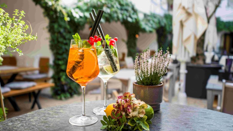 Cocktails im Maximahl, © Robert Herbst Zwei Cocktails auf einem Tisch im Freien, umgeben von Pflanzen.