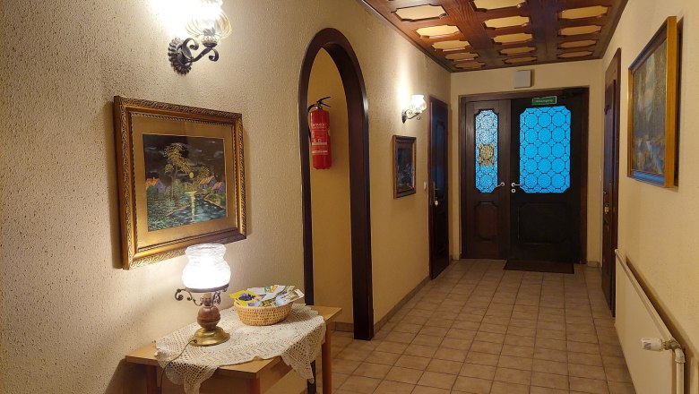 TDR-Welserhof-innen, © Nora Bartfai Innenansicht eines Flurs mit Holztisch, Lampe, Gemälden und blauen Glastüren.