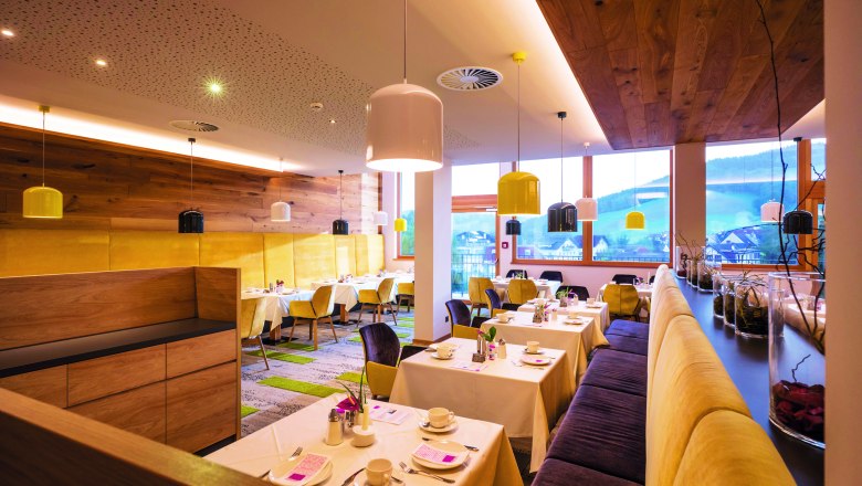 Restaurant des Vivea Hotel zum Landsknecht, © Gesundheitshotel Landsknecht Hannes Dabernig Modernes Restaurant mit Holzwänden, gelben Stühlen und bunten Lampen.