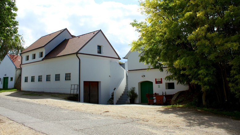 Weingut Ribisch, © Weingut Ribisch Weißes Gebäude mit rotem Dach und grünen Türen, umgeben von Bäumen.