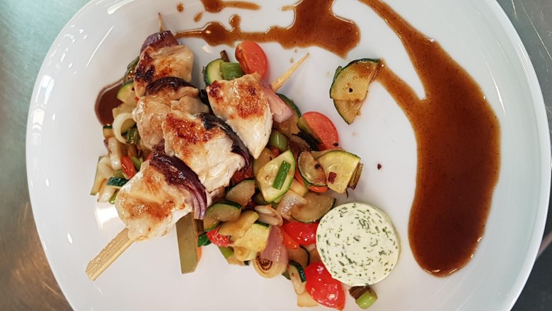 Spieße, © Reef & Beef Gegrillte Fleischspieße mit Gemüse und Kräuterbutter auf einem weißen Teller.