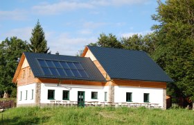 Eibl-Teichhütte, © Fam. Tröstl Eine Hütte mit Solarpanelen auf dem Dach, umgeben von Bäumen und Wiese.