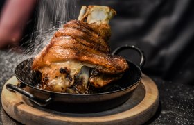 Hofbräu am Steinertor, © Extra Krems Knusprige Schweinshaxe in einer Pfanne auf einem Holzbrett, mit Salz bestreut.