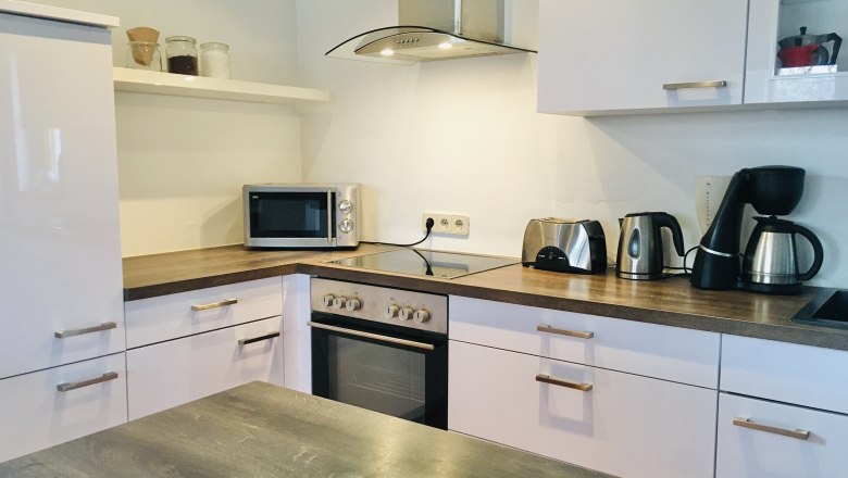 vollausgestattete Küche, © Foto: Eva Zwirner Moderne Küche mit weißen Schränken, Herd, Mikrowelle, Toaster, Wasserkocher und Kaffeemaschine.