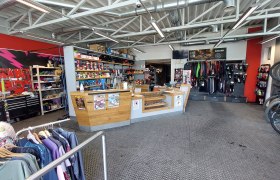 Bikestore.cc, © Bikestore.cc Innenansicht eines Fahrradgeschäfts mit Werkstattbereich, Verkaufstresen und Fahrradzubehör.