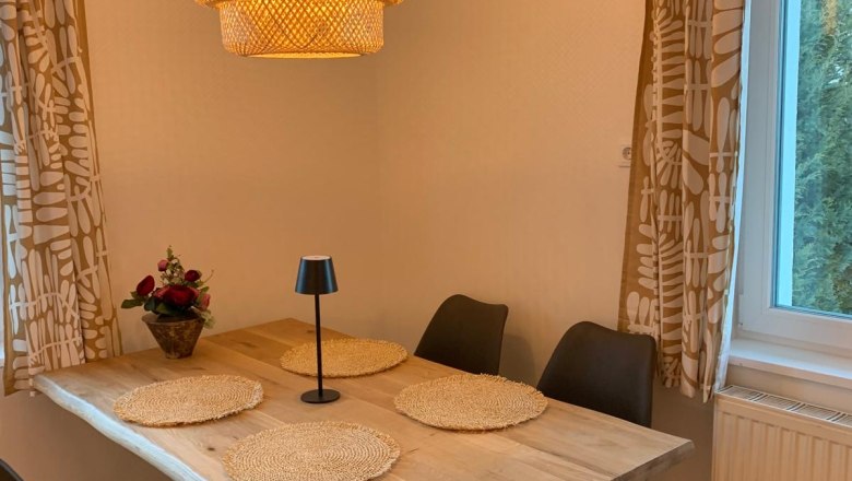 Essbereich, © Marianne Gschaider Essbereich mit Holztisch, vier schwarzen Stühlen, runder Lampe und Fenster mit Vorhängen.