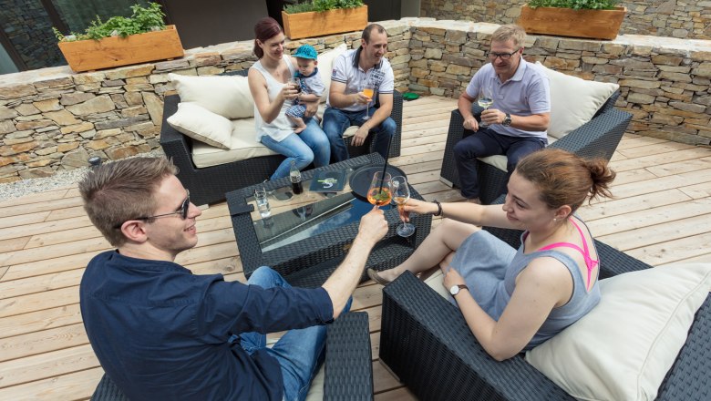 Geselliges Beisammensein auf der Terrasse, © KASTNER NEW MEDIA - kastner.tv Gruppe von Menschen sitzt aAuf einer Terrasse und stößt mit Getränken an.