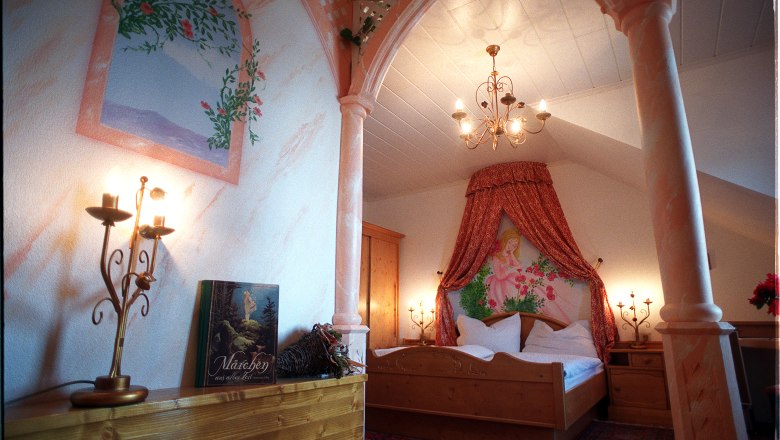 Dornröschenzimmer, © Andreas Schmidt Ein romantisch dekoriertes Schlafzimmer mit Baldachin, Kerzenleuchtern und einem Märchenbuch auf einem Regal.