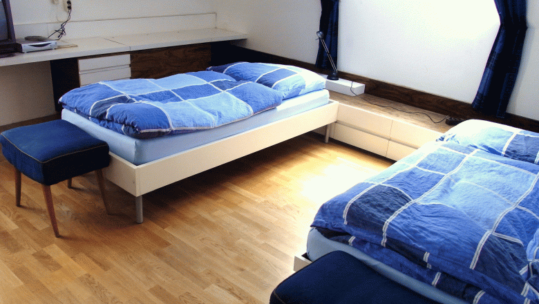 Linke Gert, Mag., © Mag. Linke Ein helles Schlafzimmer mit zwei Einzelbetten, blauen Bettdecken und einem Dachfenster.