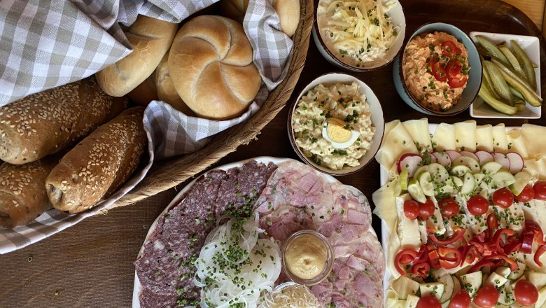 TD-Alpenvereinshaus Tulln-Brettl Jause, © Birgit Rabacher Eine Auswahl an österreichischen Jausenspezialitäten mit Brot, Aufschnitt, Käse, Salaten und eingelegten Gurken auf einem Tisch.