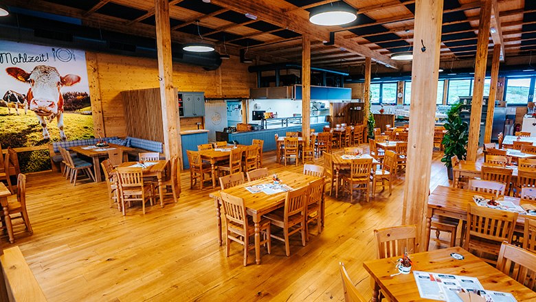 Eis-Greissler Kulinarik-Stadl innen, © Blochberger Eisproduktion GmbH Rustikales Restaurant mit Holzeinrichtung, eckigen Tischen und Stühlen sowie Säulen.