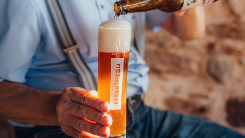 Selbstgebrautes Bier, © Niederösterreich Werbung/Daniela Führer Eine Person schenkt Bier aus einer Flasche in ein Glas mit der Aufschrift 'HaselBräu'.