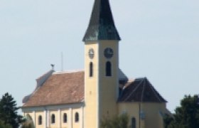 Pfarrkirche Großebersdorf, © Gemeinde Großebersdorf Pfarrkirche Großebersdorf mit spitzem Turm und Uhr, umgeben von Bäumen.