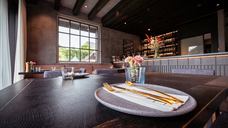 Refugium Lunz, © Niederösterreich Werbung / Maximilian Pawlikowsky Elegantes Restaurant mit gedecktem Tisch, goldfarbenem Besteck und Blumen.