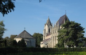 Marienkirche Bad Deutsch-Altenburg, © Marktgemeinde Bad Deutsch-Altenburg Marienkirche in Bad Deutsch-Altenburg mit blauem Himmel und Bäumen im Vordergrund.