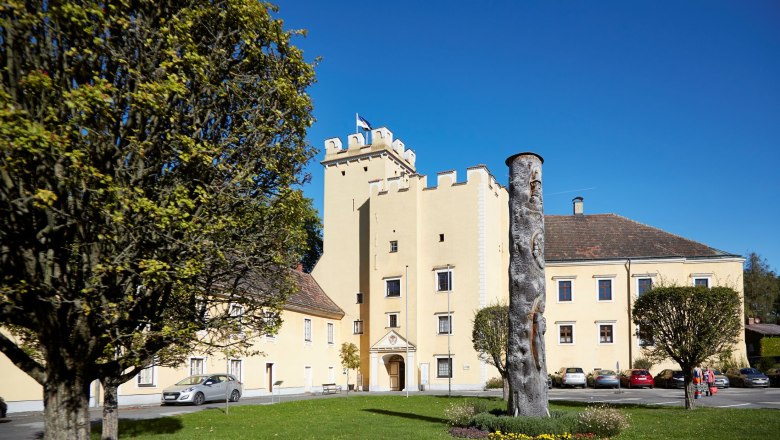 Schloss Groß-Siegharts, © Waldviertel Tourismus, lichtstark.com Schloss Groß-Siegharts mit gelbem Gebäude und Turm, umgeben von Bäumen und einer Wiese mit Skulptur.