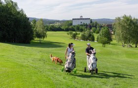 Golfclub Weitra, © www.michaelholzweber.com Zwei Golfer mit Hund auf grünem Golfplatz, Schloss im Hintergrund.