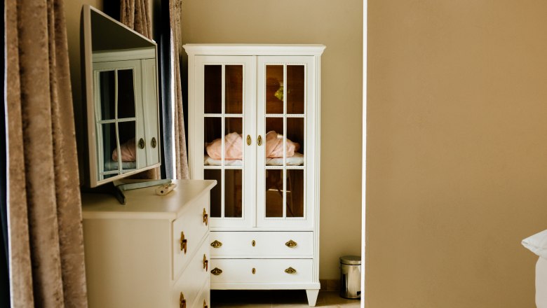 villa_schonthal-14_4, © Julius Hirtzberger Innenansicht eines Zimmers mit weißem Schrank und Kommode, Spiegel und Vorhängen.