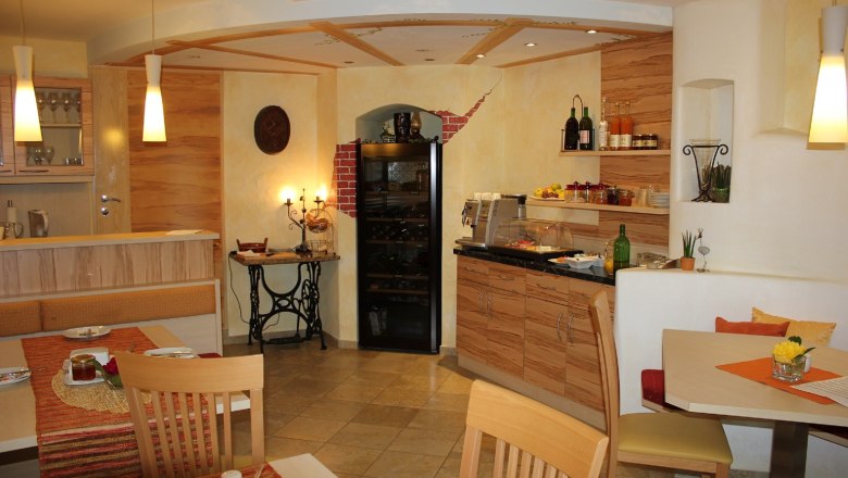 Frühstücksraum, © Gästehaus Langthaler Gemütlicher Frühstücksraum mit Holzmöbeln, gedeckten Tischen und einem Buffet mit Getränken und Speisen.