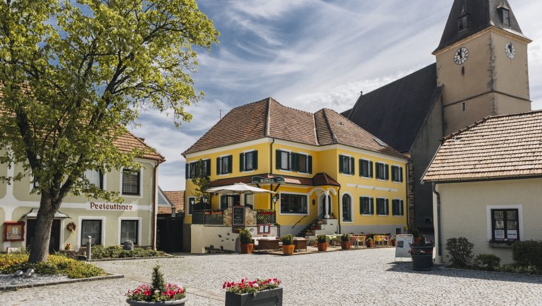 Einkehren in Maria Laach, © Niederösterreich Werbung/David Schreiber Idyllischer Dorfplatz mit Gasthaus und Terrasse und ein Kirchturm im Hintergrund.