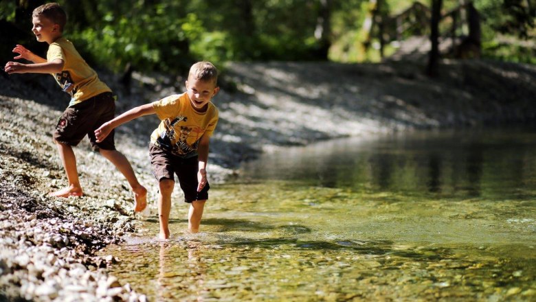 Erlebniswelt Mendlingtal, © weinfranz.at Zwei Kinder spielen am Ufer des klaren Wassers in der Natur.