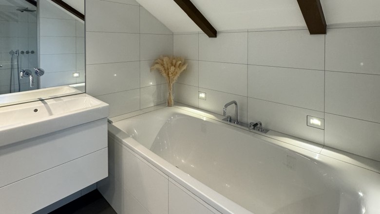 Badezimmer, © Juwel am Stadtrand Modernes Badezimmer mit Badewanne, Waschbecken und schräger Decke mit Holzbalken.