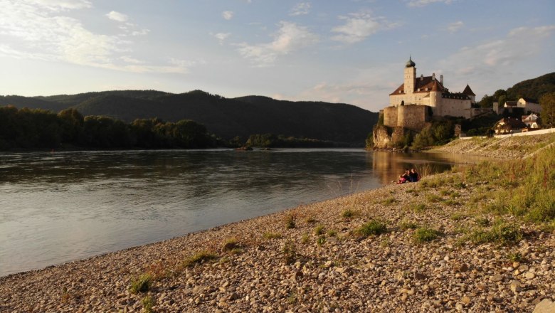 Badestrand an der Donau vor dem Areal, © Szilágyi Kiesstrand an der Donau mit Burg im Hintergrund bei Sonnenuntergang.