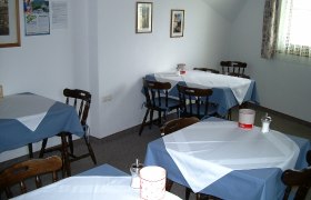 Frühstücksraum, © Mang Lieselotte Ein Frühstücksraum mit mehreren Tischen, die mit blauen und weißen Tischdecken gedeckt sind.