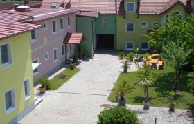 Pension Geyer, © Pension Geyer Innenhof einer Pension mit bunten Gebäuden, Pflanzen und Sitzbereich.