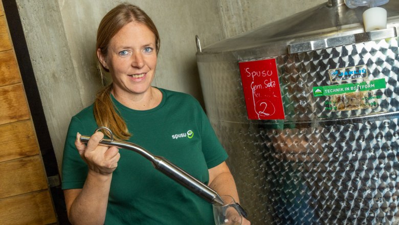 Veronika Pichler, Geschäftsführerin, © spusuwein Eine Frau in einem grünen T-Shirt steht neben einem großen Edelstahltank und hält ein Glas mit einer Flüssigkeit.