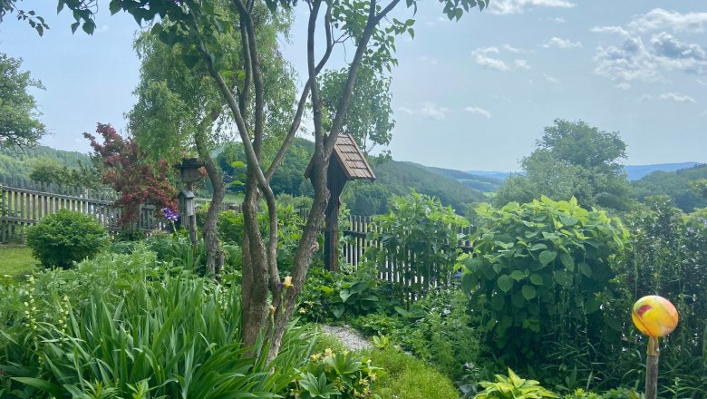 Ferienwohnungen Riedl, © Wiener Alpen Ein grüner Garten mit Bäumen, Sträuchern und einem Holzzaun im Hintergrund.