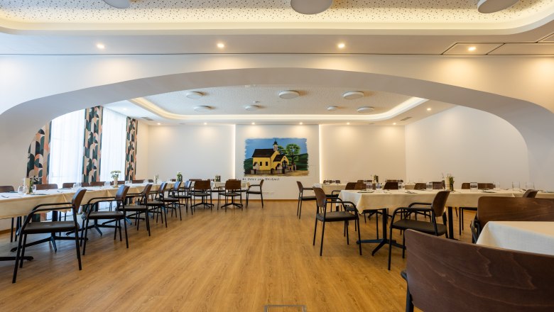 Innenansicht Wirtshaus, © Lucas Suhane Innenansicht eines modernen Wirtshauses mit gedeckten Tischen und einem Wandgemälde.