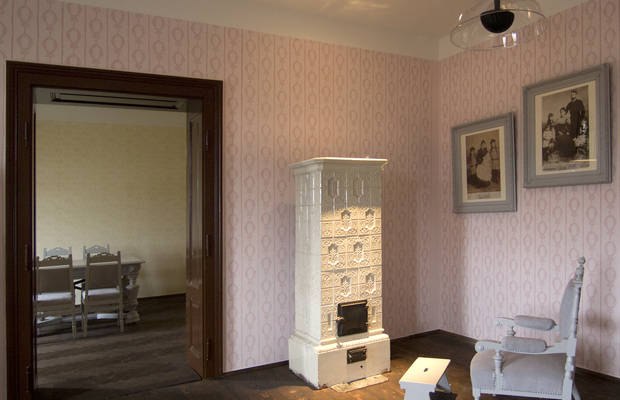 Geburtshaus Egon Schiele, © Stadtgemeinde Tulln, Hans Eder Innenansicht eines Raumes mit antikem Ofen, zwei gerahmten Bildern und einem Stuhl.