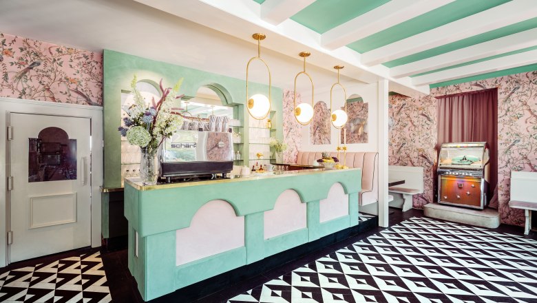 Fernblick, © Matthias Kronfuss Innenansicht eines stilvollen Cafés mit pastellfarbenem Dekor, geometrischem Bodenmuster und einer Jukebox.